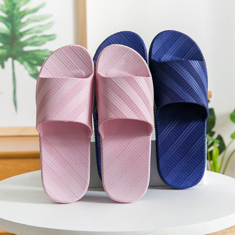Pair of pink and blue striped slippers on a white surface with a plant in the background.
