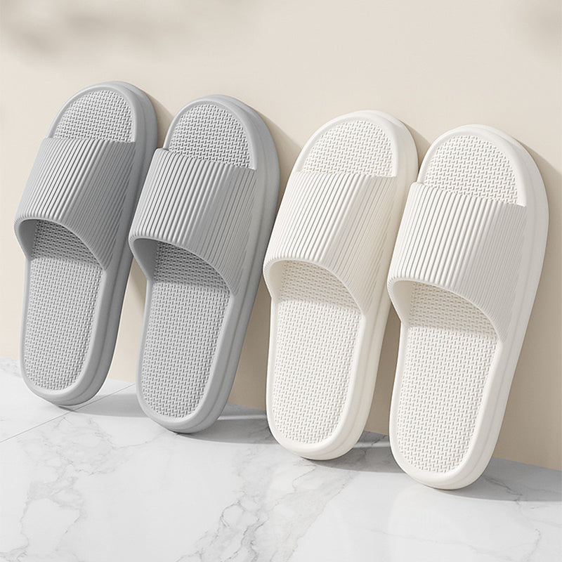 Two pairs of gray and white slippers on a marble surface with a beige wall background.