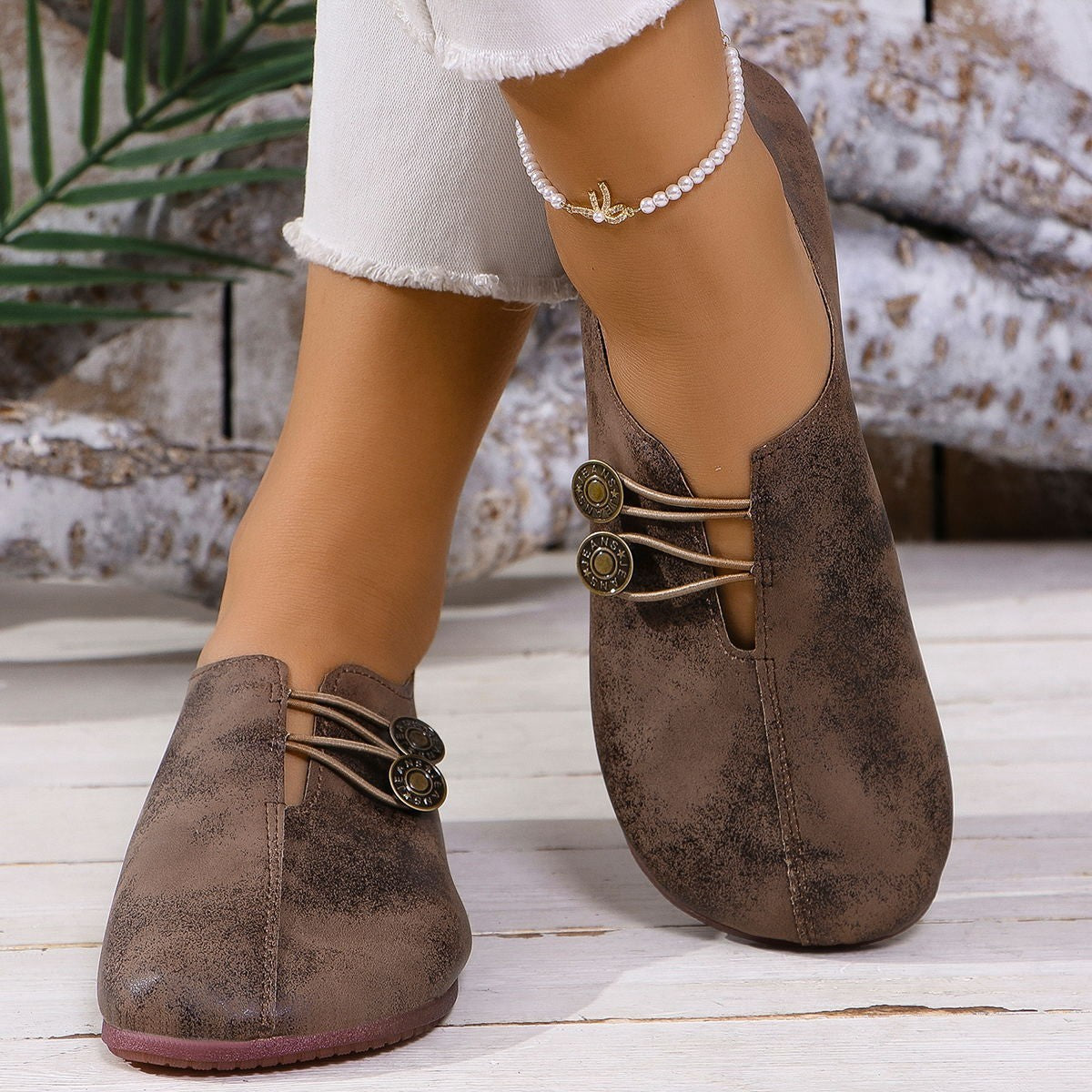Brown suede shoes with decorative laces worn by a person on a wooden floor.