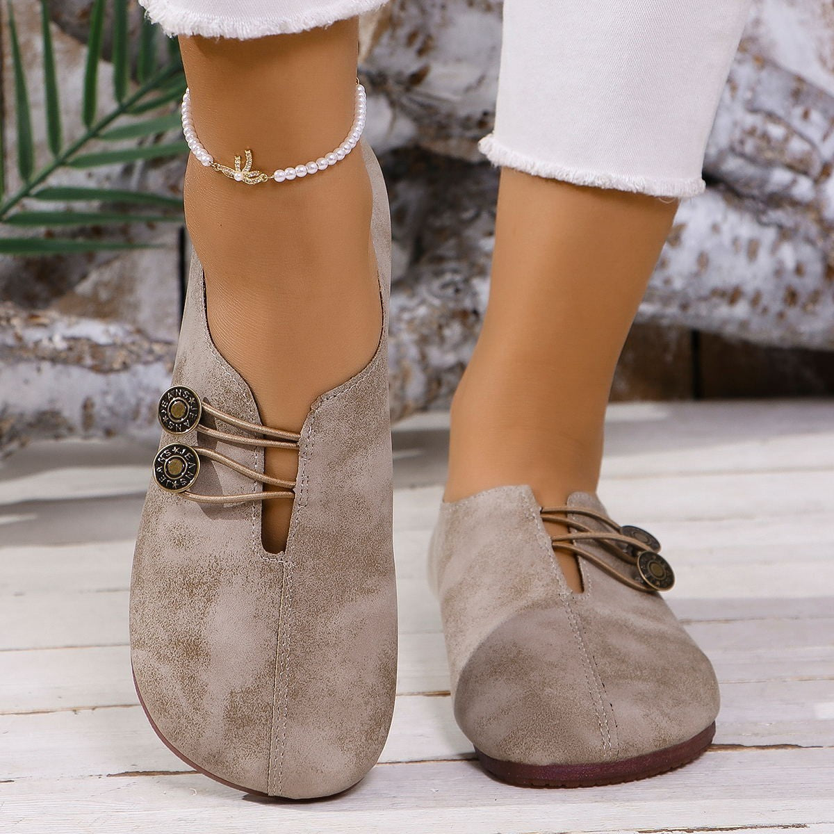 Beige suede shoes with brown soles worn by a person on a wooden floor.