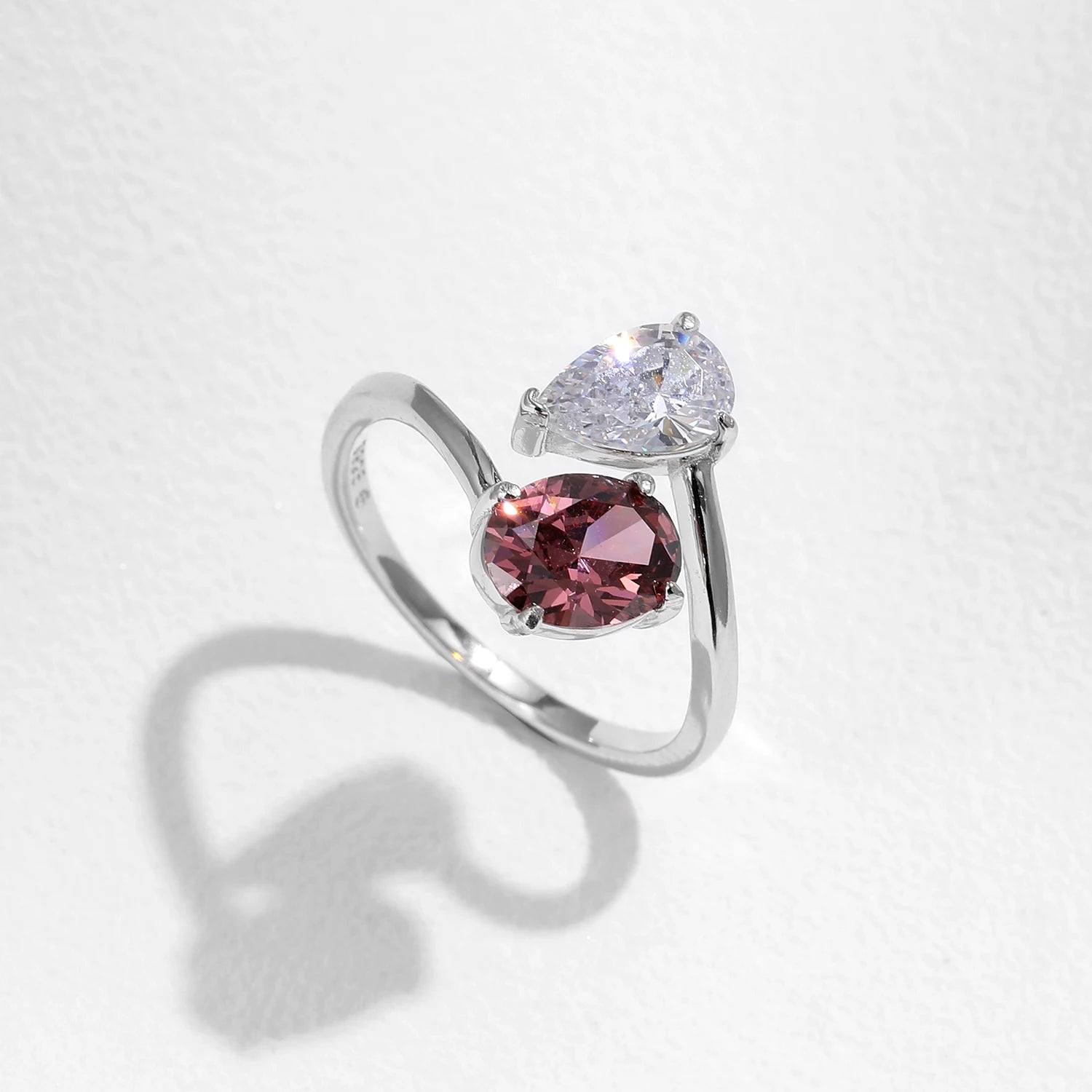 Silver ring with a pink gemstone and clear stone on a light gray background