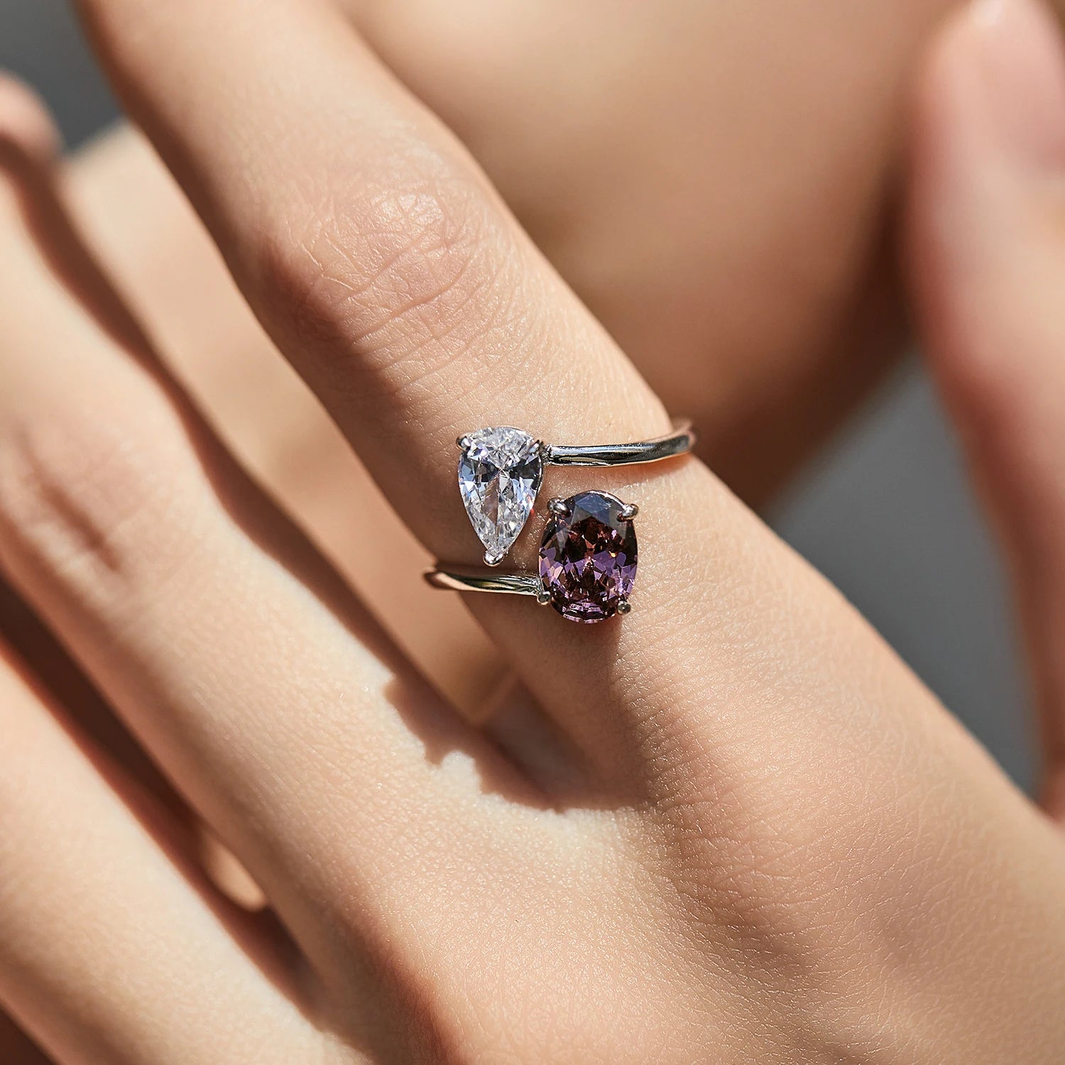 Close-up of a hand wearing two rings with gemstones on a neutral background