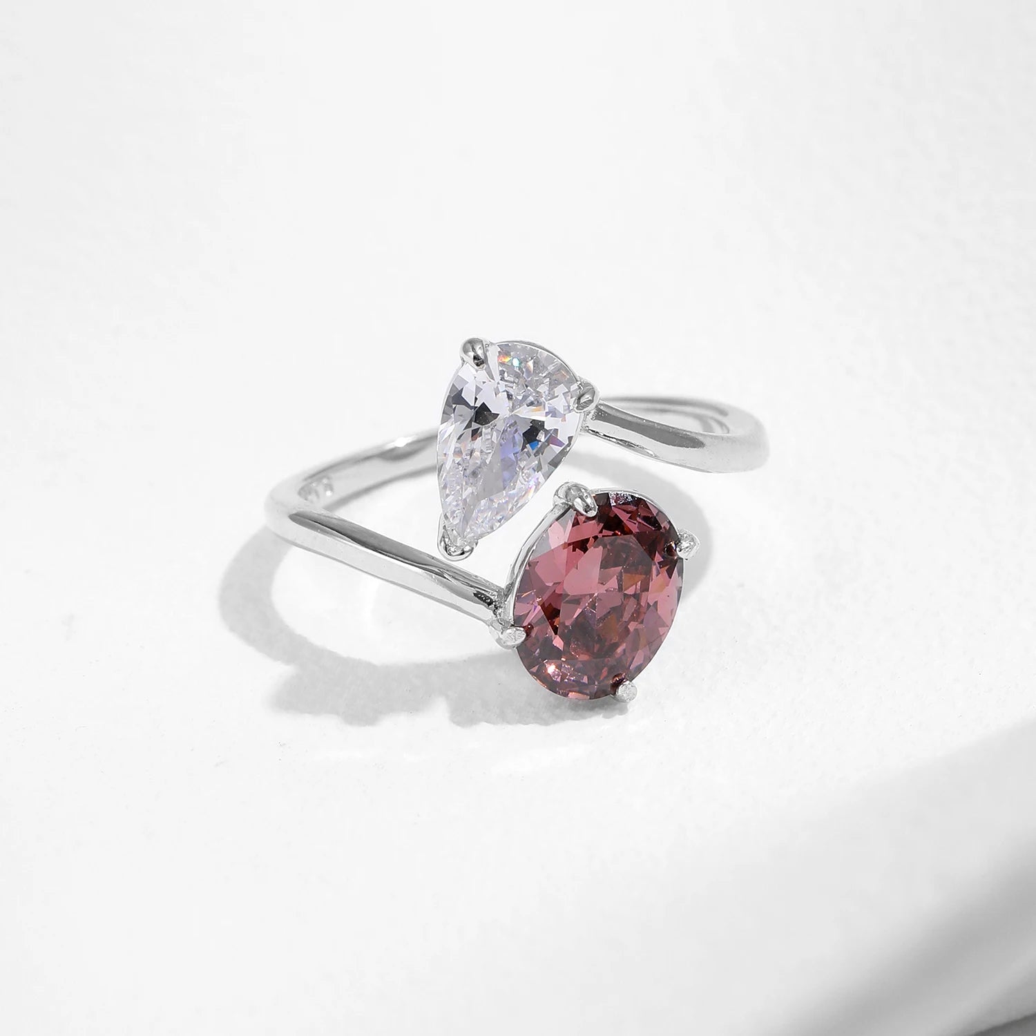 Silver ring with a pear-shaped white gemstone and a pink gemstone on a light gray background